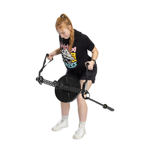 A red-haired woman in a ponytail uses the Bells of Steel 30 D-Handle Bar Cable Attachment with Carabiners. She wears a black t-shirt with a colorful design, black shorts, and white sneakers, standing against a white background.