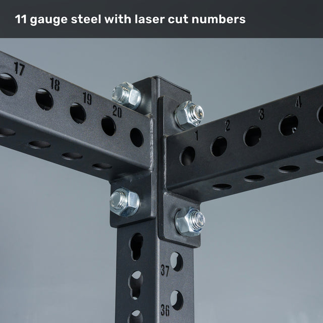 Close-up of black steel beams from the Bells of Steel Manticore Four Post Power Rack – Prebuilt (3" x 3", 1" Holes), featuring laser-cut numbered holes and large silver bolts at the intersections. Text above reads, “11 gauge steel with laser cut numbers.” This modular rack delivers a durable, customizable foundation engineered for strength in your home gym.