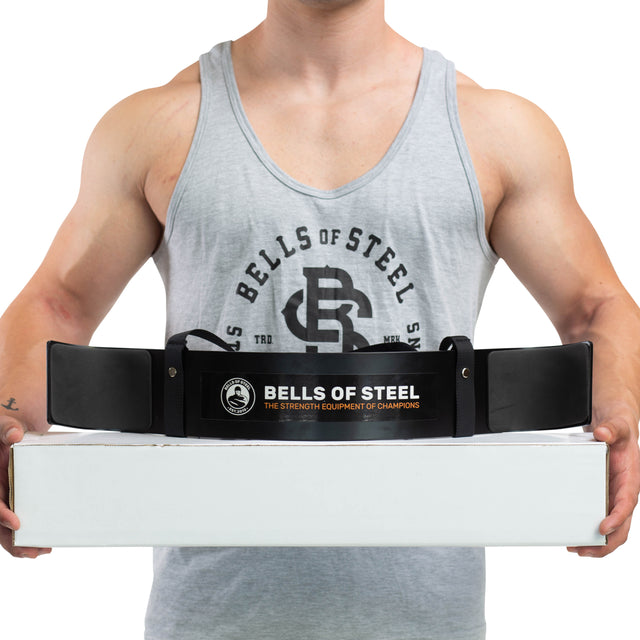 A person in a grey Bells of Steel tank top holds a white box with a black Bells of Steel Arm Blaster draped over it, ready for an intense biceps workout.