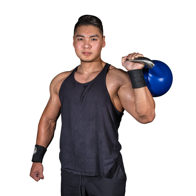 A muscular man wears Bells of Steel BellGuard Kettlebell Wrist Guards and a black tank top, holding a blue kettlebell on his shoulder against a white background—showcasing wrist protection for serious lifters.