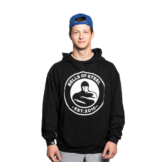 A young man wearing a blue backwards cap and a black Bells of Steel Bamboo Hoodie stands facing forward against a plain white background.
