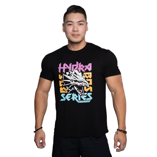 A man with short hair wears the Bells of Steel Bamboo T-Shirt, a black, sweat-wicking gym shirt featuring a stylized dragon and bold, colorful "Hydra Beats Series" text, standing confidently against a white background.