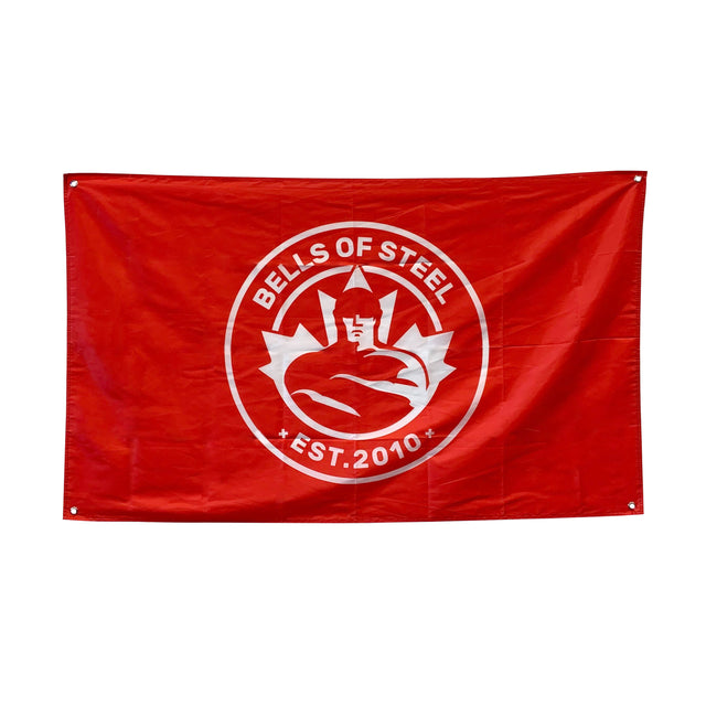 Display the Bells of Steel Flags—a red flag with a white circular logo featuring a muscular figure, maple leaf, and "BELLS OF STEEL EST. 2010"—perfect gym decor to upgrade your home gym.