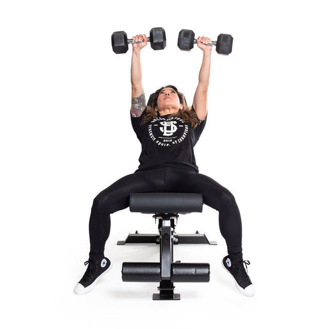A woman in workout clothes lies on a bench, performing a bench press with two Bells of Steel Ergo Rubber Hex Dumbbell Sets against a plain white background.