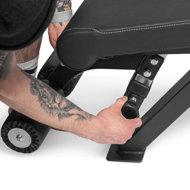 A tattooed arm adjusts the pin on a Bells of Steel Flat/Incline/Decline Weight Bench - Commercial, showcasing its padded seat and sturdy metal frame, perfect for versatile muscle-targeting exercises.
