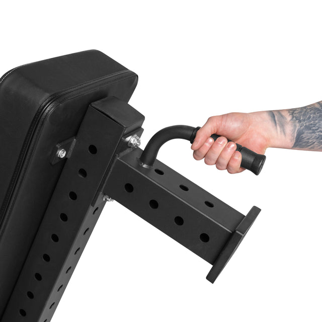 A tattooed hand adjusts the Bells of Steel Powerlifting Flat Bench, featuring a sleek black cushion, by turning a lever on its metal frame with evenly spaced holes. This light commercial grade bench supports up to 1,000lb max capacity.