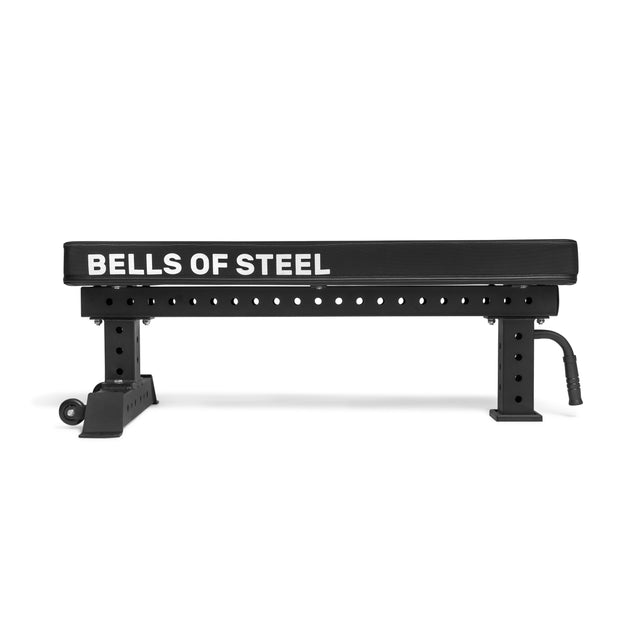 The Powerlifting Flat Bench by Bells of Steel is a black adjustable exercise bench with a sturdy steel frame and multiple adjustment holes for different heights. It features a flat, padded surface ideal for weightlifting and other fitness routines.