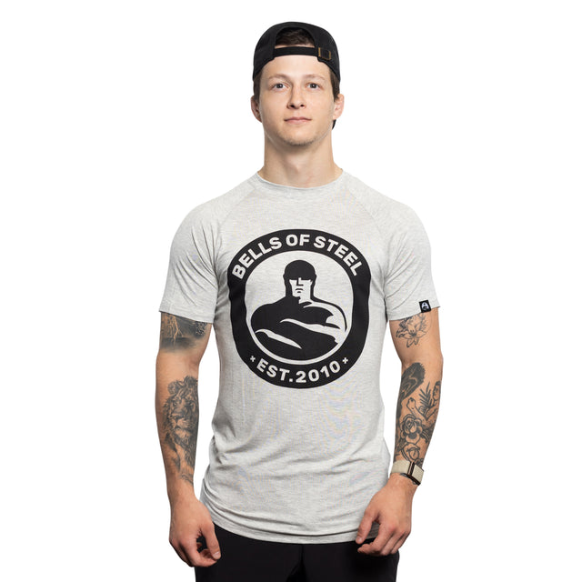 A man in a backward black cap and light gray Bells of Steel Bamboo T-Shirt stands facing forward, displaying tattooed arms, against a plain white background.