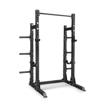 The Bells of Steel Manticore Half Rack – Prebuilt is a black metal power rack designed for weightlifting, featuring sturdy 3" x 3" uprights with precise 1" holes for adjustable barbell height, safety bars, a pull-up bar at the top, and convenient weight plate storage pegs on the sides—making it an ideal addition to any home gym. This versatile rack stands prominently on a white background.