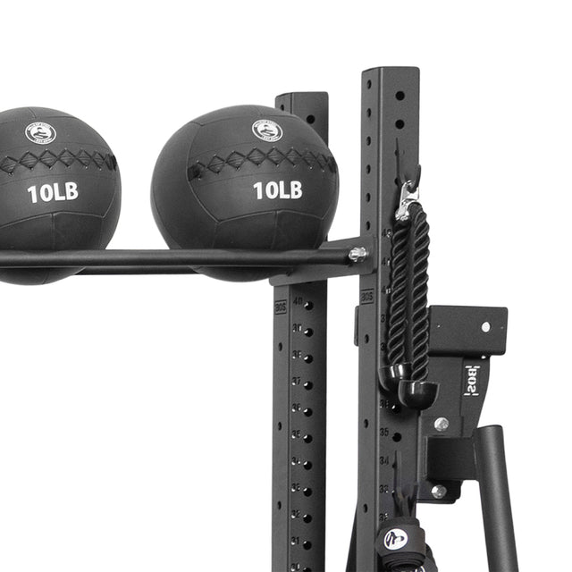 Two black 10-pound medicine balls rest on a metal rack featuring the Bells of Steel Utility Hook, with a tricep rope hanging nearby and an iPad holder partially visible on the sideâan efficient gym storage solution.