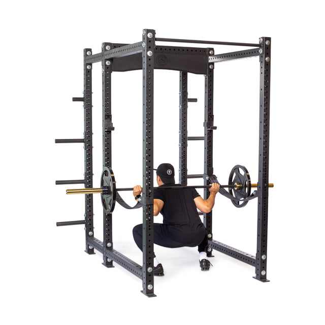 A person in black workout gear does a barbell squat inside the Bells of Steel Hydra Six Post Power Rack (3" x 3", ⅝" holes), fully loaded with weight plates—an ideal addition to any home gym.