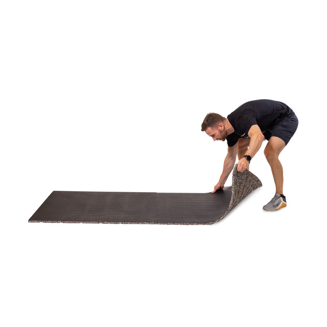 A man in athletic wear unrolls the Bells of Steel Rubber Flooring Gym Mat 39" x 39" on a white background, showcasing its sound dampening features.