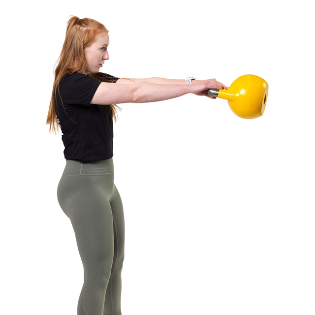 A woman in athletic wear stands in profile against a white background, lifting a yellow Bells of Steel Competition Kettlebell with both hands out in front of her.