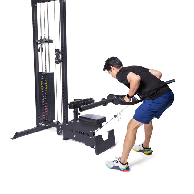 A man uses the Bells of Steel Lat Pulldown Low Row Machine with a bar attachment, wearing a black shirt, blue shorts, and sneakers. He pulls the bar to his torso, highlighting an effective cable row for strength training.