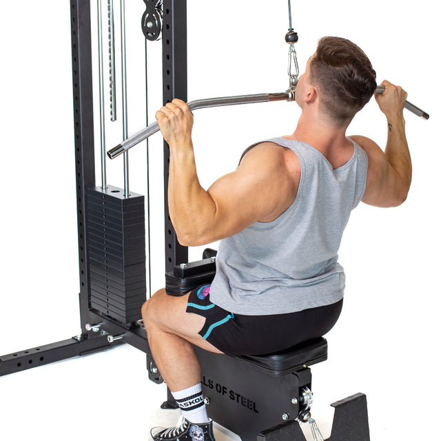 A man in a gray tank top and black shorts uses the Bells of Steel Lat Pulldown Low Row Machine, demonstrating effective cable exercises at the gym.