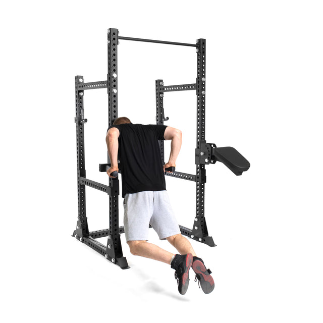 A person in a black shirt and gray shorts performs dip exercises on Bells of Steel's Manticore Half Rack - Prebuilt (3" x 3", 1" Holes), set up against a white background for a home gym.