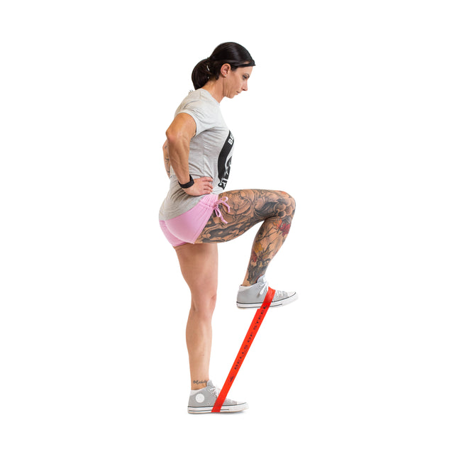 A woman in athletic wear demonstrates Bells of Steel Mini Bands, stepping on the band and lifting her knee with hands on hips, against a white background—highlighting these versatile gym accessories.