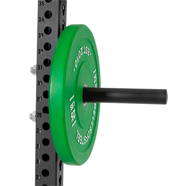 A green weight plate sits on a Bells of Steel Bolt-On Plate Peg Set, a black storage solution designed for efficient plate organization on metal power racks with numbered holes.