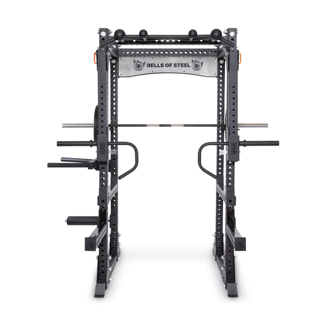The Bells of Steel Manticore Flat Foot Power Rack - Prebuilt (3" x 3", 1" Holes) features a black steel frame, attachments, weight plate holders, and a pull-up bar. The top banner displays "BELLS OF STEEL" with ram head logos on each side.