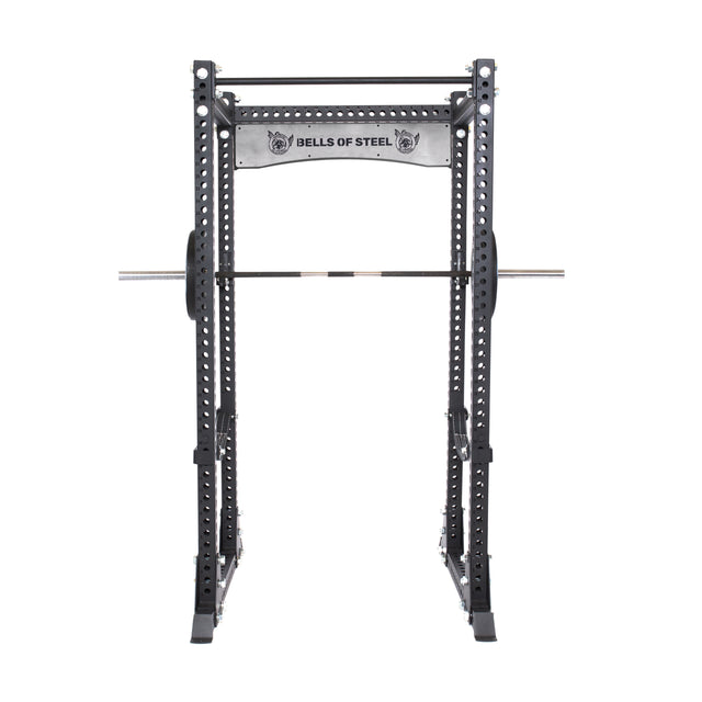 A Bells of Steel Manticore Flat Foot Power Rack - Prebuilt (3" x 3", 1" Holes) in black, with multiple adjustment holes, pull-up bar, and barbell on the side hooks, is shown against a plain white background—ideal for any home gym.