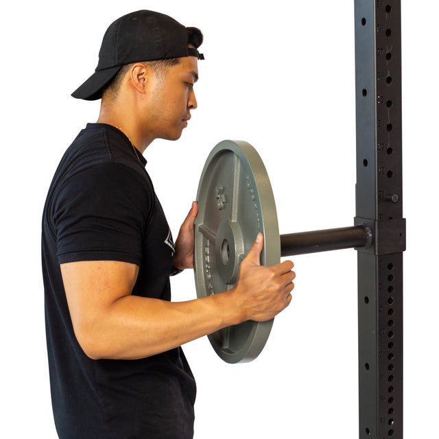 A man in a black t-shirt and backwards cap loads a weight plate onto a barbell attached to a squat rack fitted with Bells of Steel Pin Plate Pegs for convenient Olympic weight plate storage.