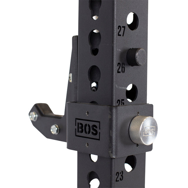 Close-up of Bells of Steel Sandwich J-Cups on a black squat rack with numbered holes and a silver knurled adjustment knob—heavy-duty accessories for secure, stable lifts.