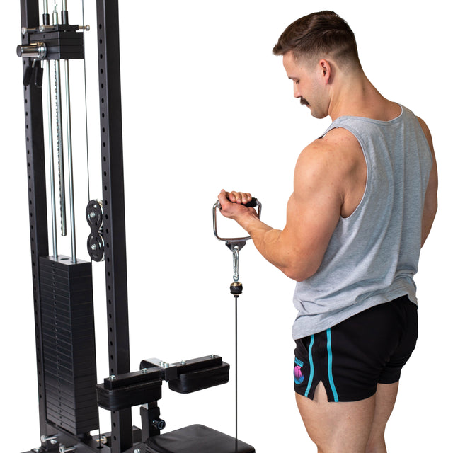 A man in a gray tank top and black shorts performs a tricep exercise on a cable machine, gripping the Bells of Steel Single D Handle Cable Attachment with both hands while facing the equipment.