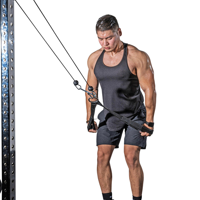 A man in a black tank top and shorts uses the Bells of Steel RocIT Tricep Strap on a cable machine, gripping it with both hands while performing a triceps pushdown against a white background.