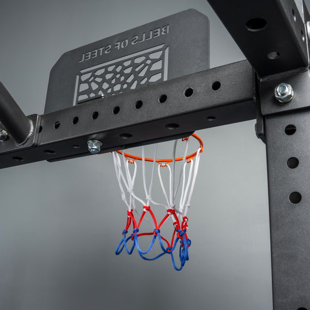 A close-up of the Bells of Steel Rack Attached Basketball Hoop w/ Ball, featuring a red, white, and blue net on a black frame with "BELLS OF STEEL" on the backboard, designed as a power rack attachment for home gyms.