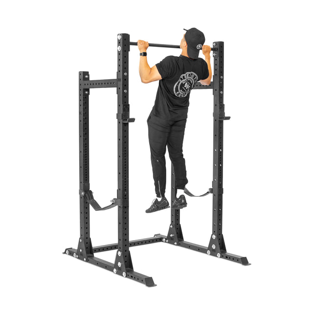 A person in black athletic clothing does a pull-up on the Bells of Steel Hydra Half Rack - Prebuilt (3" x 3", ⅝" holes), viewed from the back against a white background—perfect for any home gym.