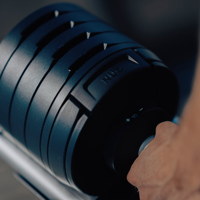 Close-up of a hand gripping the NÜOBELL-S Adjustable Dumbbell by Bells of Steel, featuring clear weight settings, smooth dial adjustment, and a sleek black design—ideal for any home gym.