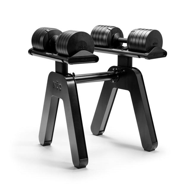 A pair of NÜOBELL-S adjustable dumbbells sits on the Bells of Steel NÜOBELL-S Floor Stand, featuring sturdy black legs and set against a white background.