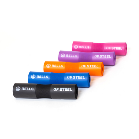 Five foam barbell pads in black, blue, orange, purple, and pink are arranged diagonally on a white background. Each pad is labeled “BELLS OF STEEL.”.