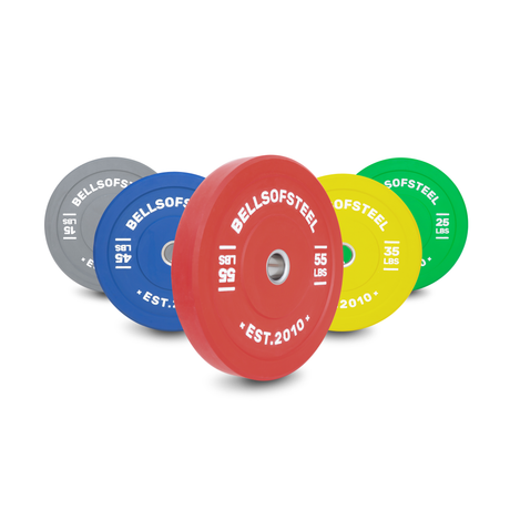 Five colorful weight plates labeled "BELLSOFSTEEL" in gray, blue, red, yellow, and green are standing upright in a row, each with its weight in pounds marked on the front.