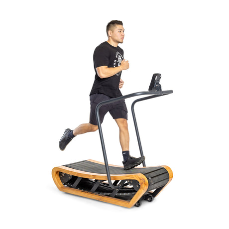 A man in black athletic wear runs on a wooden curved treadmill with a digital display against a white background.