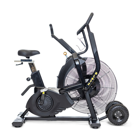 A black air bike exercise machine with a large front fan wheel, footrests, pedals, moving handles, and an adjustable seat, shown in a side view on a white background.