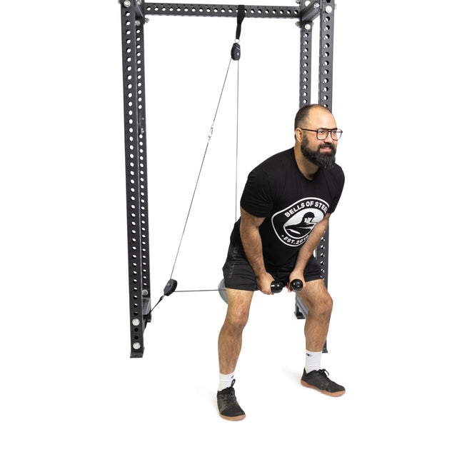 A man with a beard and glasses uses the Bells of Steel Tricep Rope Extension for a cable front raise in a squat stance, wearing a black t-shirt, shorts, white socks, and sneakers.