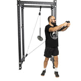 A bearded man with glasses demonstrates the Bells of Steel Tricep Rope Extension on a cable machine, wearing a black t-shirt, black shorts, and sneakers against a plain white background.