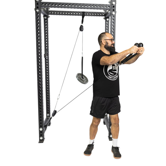 A bearded man with glasses demonstrates the Bells of Steel Tricep Rope Extension on a cable machine, wearing a black t-shirt, black shorts, and sneakers against a plain white background.