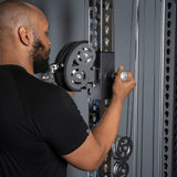 A man in a black shirt adjusts the handle of a Bells of Steel Oblivyon Tower - 3" x 3” Cable Tower, tightening it on the metal exercise machine.