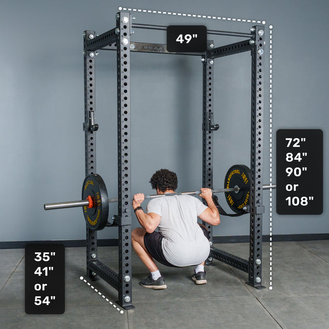 A person is squatting inside the Bells of Steel Manticore Four Post Power Rack Builder (3" x 3", 1" holes), a black power rack with labeled dimensions: width 49", selectable height options from 72" to 108", and depth options between 35" and 54". Two weight plates are loaded on a barbell, showcasing the versatile setup of this customizable power rack.
