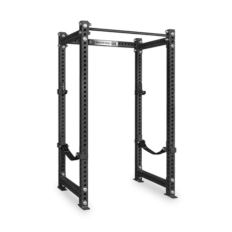 The Bells of Steel Manticore Four Post Power Rack - Prebuilt features sturdy 3" x 3" uprights with 1" holes for adjustable attachments, reinforcing bars, and safety straps. Designed for weightlifting and strength training in your home gym, this black steel power rack stands out against a white background.