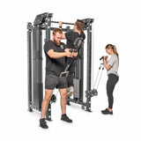 Three people are using the Kraken Rack Attachment for 4 Post Hydra & Manticore Racks by Bells of Steel. A man assists another with pull-ups, while a woman curls a resistance band. The dual-handle cable tower has versatile pulleys and sturdy frames for diverse workouts.