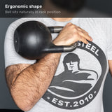 A person holds a Bells of Steel 6-12KG Adjustable Kettlebell, competition-style and black in color, in the rack position against their chest. They wear a gray t-shirt featuring a graphic of a muscular figure and the text “STEEL EST. 2010.”.