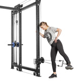 A woman in athletic wear uses the single-side Kraken Rack Attachment from Bells of Steel on a 6 Post Manticore Rack. She's in a gray T-shirt and black leggings, bracing with one hand as she extends her leg backward, utilizing the adjustable trolleys for resistance.