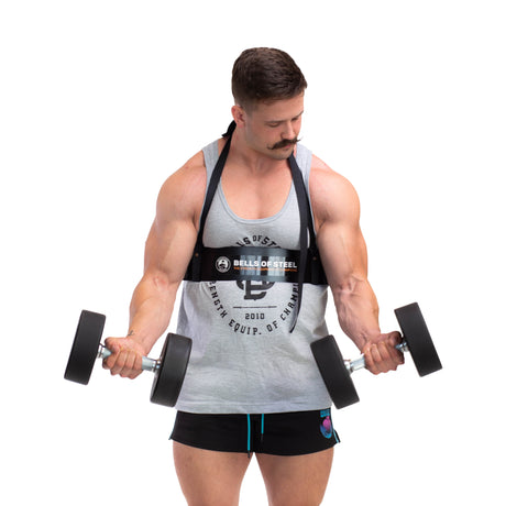 A muscular man with a mustache, in a tank top and shorts, uses the Bells of Steel Arm Blaster to perform bicep curls with dumbbells against a white background.