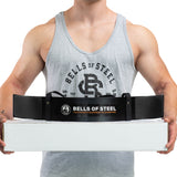 A person in a grey Bells of Steel tank top holds a white box with a black Bells of Steel Arm Blaster draped over it, ready for an intense biceps workout.