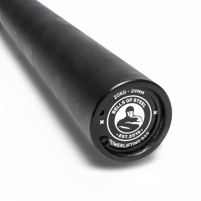 Close-up of the Bells of Steel Powerlifting Bar, featuring "Bells of Steel," "20KG - 29MM," and "Powerlifting Bar" logos. This budget-friendly bar meets IPF specs and stands out against a white background.