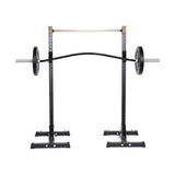 A Bells of Steel Curved Squat Bar setup with a black squat rack, adjustable safety bars, and weight holders on a white background is designed to alleviate joint stress during workouts.