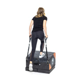 A woman in athletic wear uses the Bells of Steel Soft Glute Bench with attached resistance bands, ideal for hip thrusts and home workouts, shown against a white background.